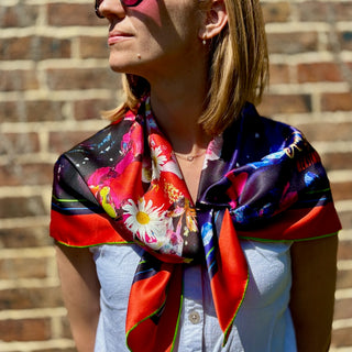 Model wearing rose tinted glasses, standing in front of a brick wall weaing the Crystal Petal Papllion Square Silk Scarf.