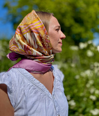 Female model wearing the Derby Pattern 188 scarf as a headscarf under sunlight with foliage