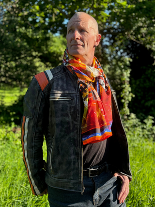 Red orange and black patterned long silk scarf worn as a wrap around scarf with a leather biker jacket.