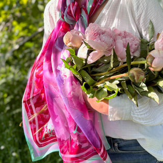A Close-up of model wearing long silk scarf over casual evening wear blouse carrying pink peonies.