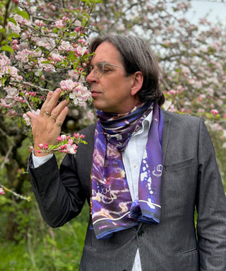 Male model wearing Blue Avon Serenity scarf loosely while smelling apple blossom, embodying peace and presence