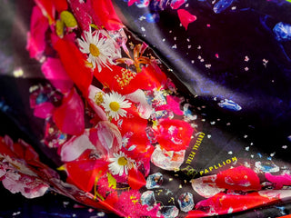 A close up of the First Audacity silk scarf, showing ox eye daisies and red petals on a dark midnight background.