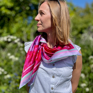 Love Peony Silk Scarf styled in a side knot over a white top, highlighting the vibrant fuchsia and delicate lilac border