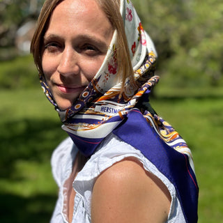Model wears The Northumbria Silk Scarf as a headscarf, front view showing elegant blue and gold detailing.