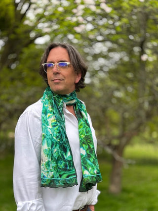 Smiling male model wearing the Green Red Sea Long Silk Scarf, by Anna Acciarini, in a wooded glade.